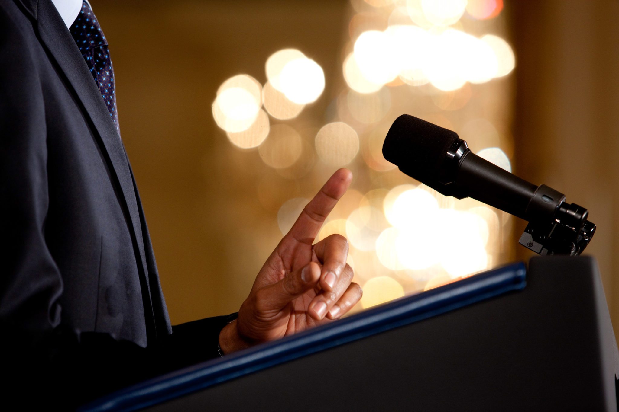 0519-0908-0820-3533_close_up_of_a_man_making_a_point_during_a_speech_microphone_and_podium_in_view_o